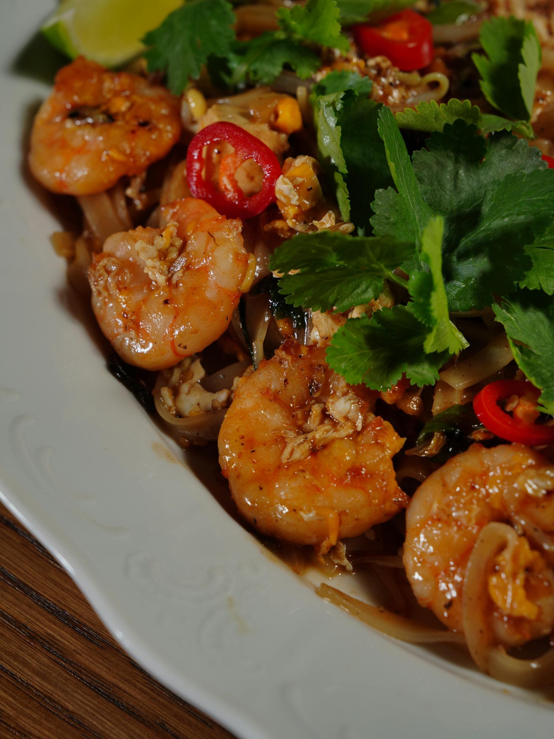 Close-up of flavorful shrimp pad thai topped with chili and cilantro, perfect for food lovers.