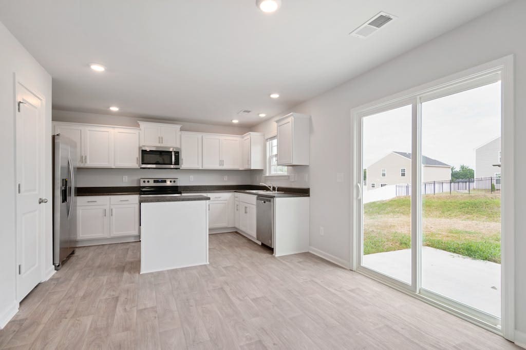 Bright and modern kitchen interior with white cabinets, island, and sliding doors to backyard.